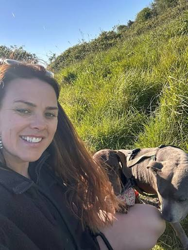 Jenna sitting in long grass with two dogs on a sunny walk