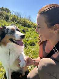Jenna holding paws with a happy collie on a hillside